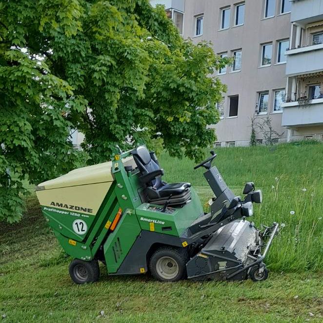 Rasenmahd Wohnungsbaugesellschaft, Greiz, Vogtland Ein grünes Rasenmäherfahrzeug steht auf einer Wiese neben einem Wohngebäude.