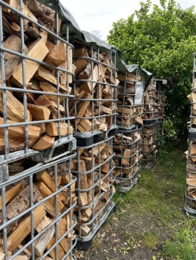 Stapeln von Holzscheiten in Gittercontainern, umgeben von Vegetation.